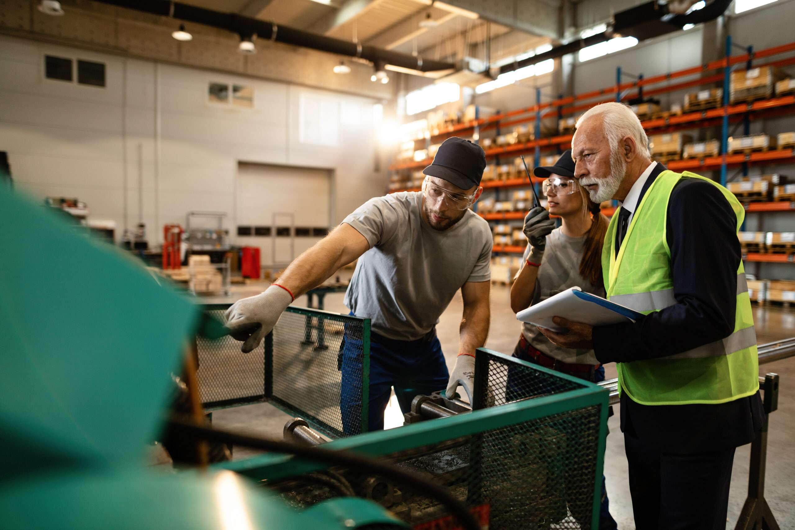 Warehouse workers showing industrial machine they are working on to their senior manager